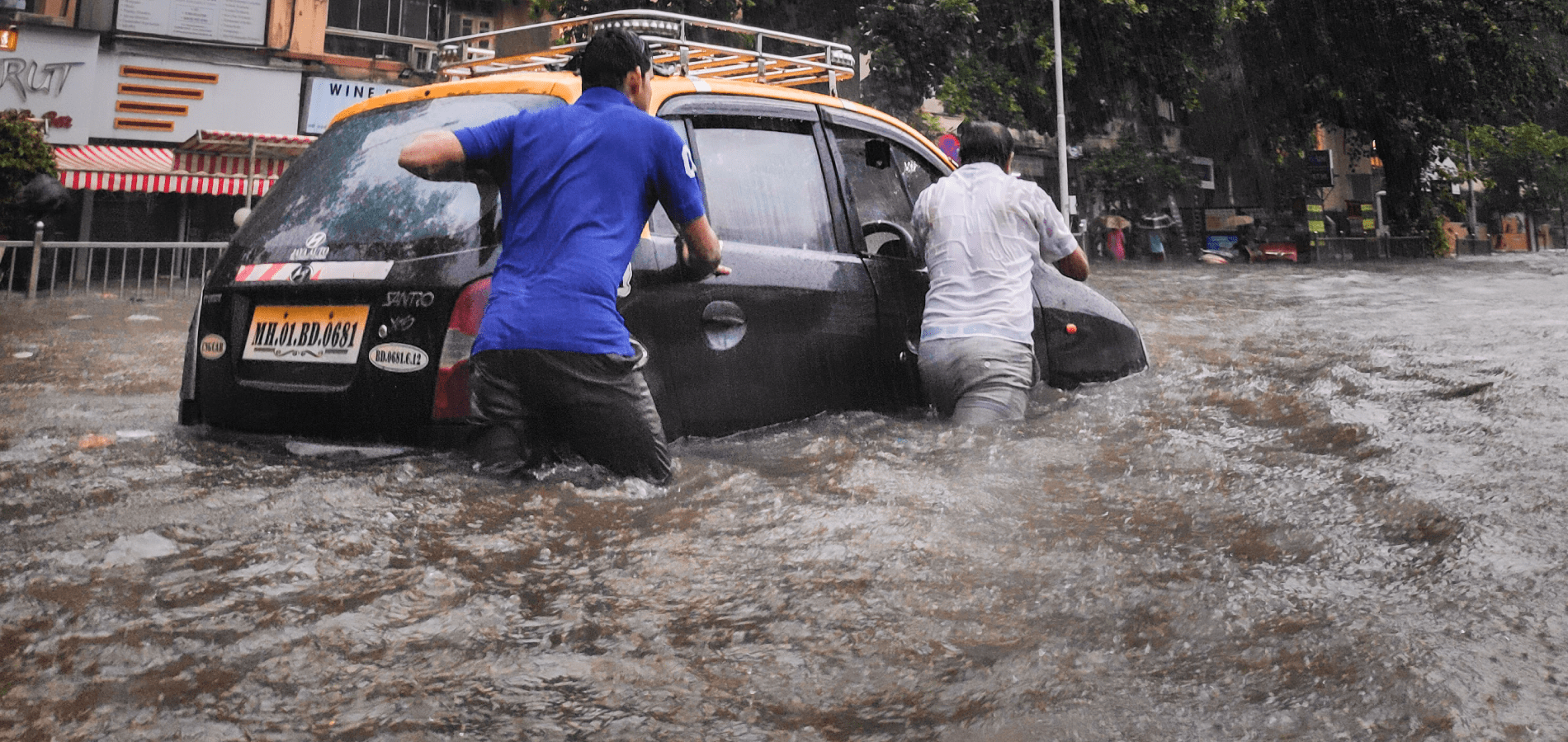 Two men pushing a car through flooded roads