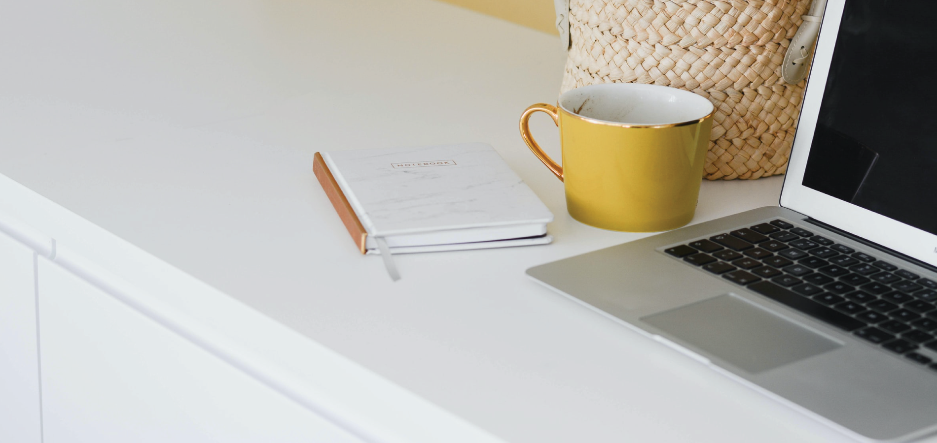 Laptop next to yellow mug on white desk