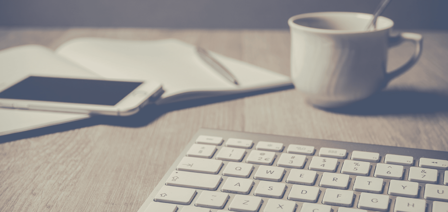 keyboard, notebook, phone and mug on a desk