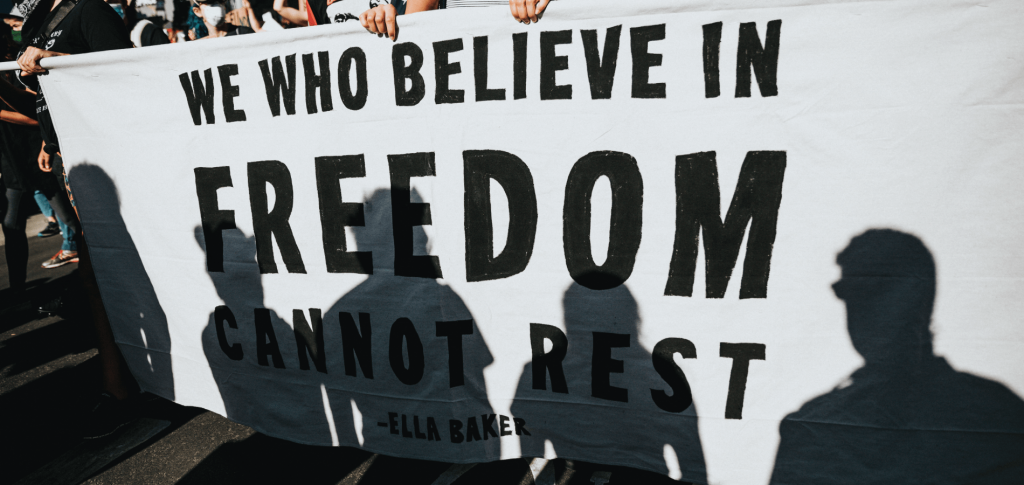 protesters carrying a sign with from Ella Baker: "We who believe in freedom cannot rest"