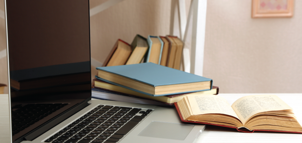 photo of laptop and books on a desk in front of a bookcase