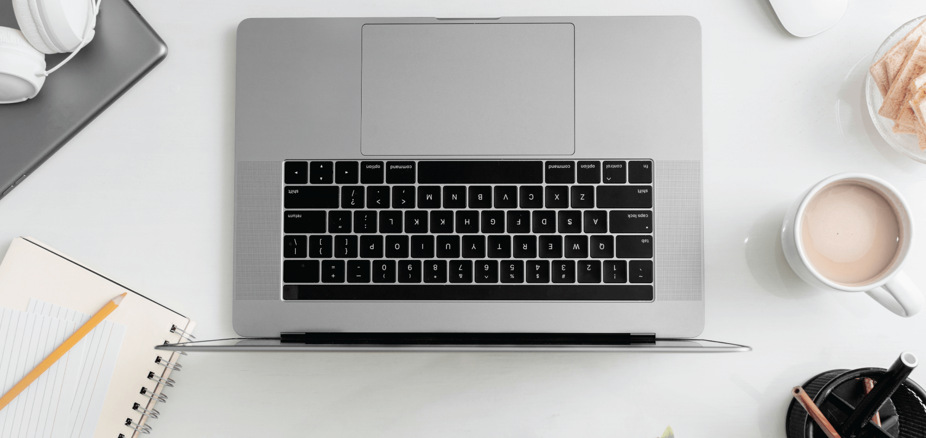 laptop on desk with notebook, headphones, cup of coffee, and pencil holder