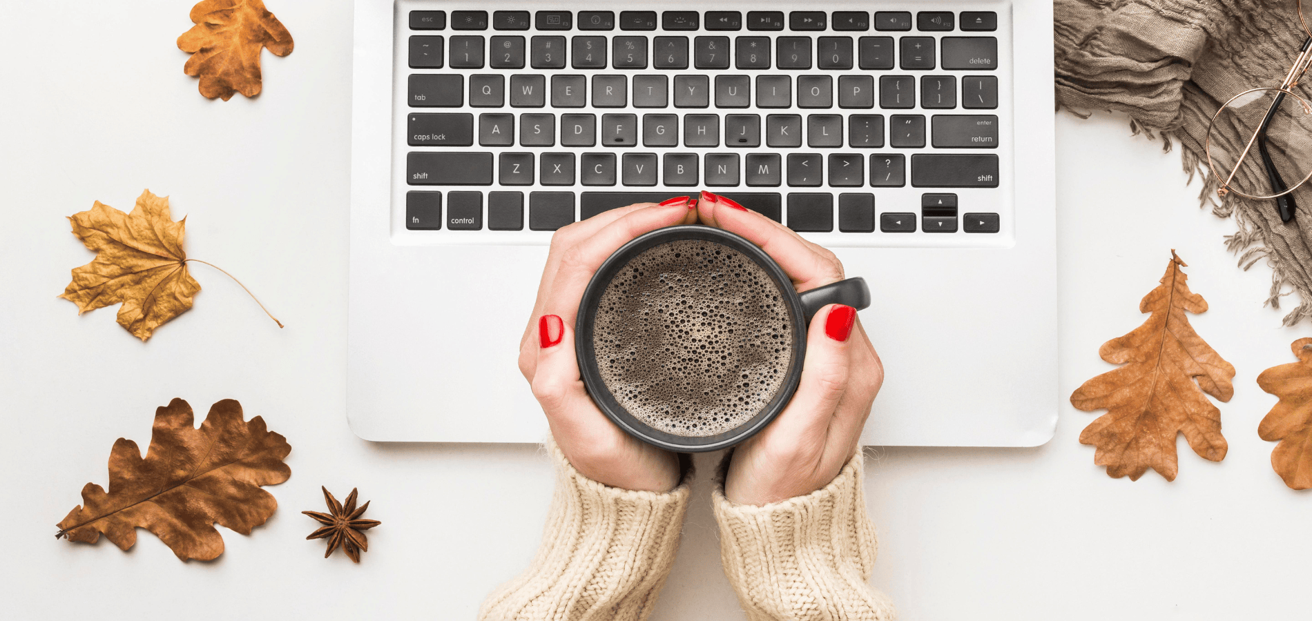 computer with a hand holding a coffee mug and orange leaves