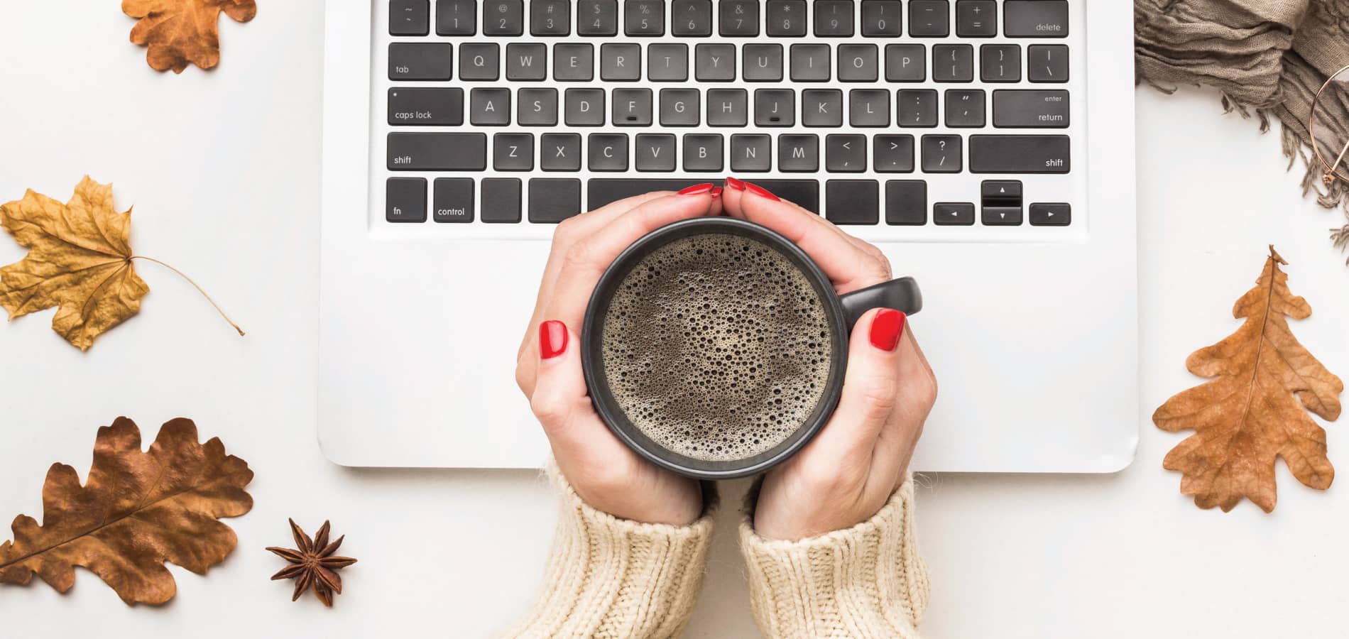 image of two hands holding coffee cup near a laptop with fall leaves