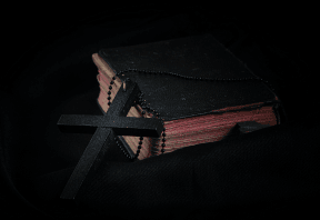Black cross leaning against black old book