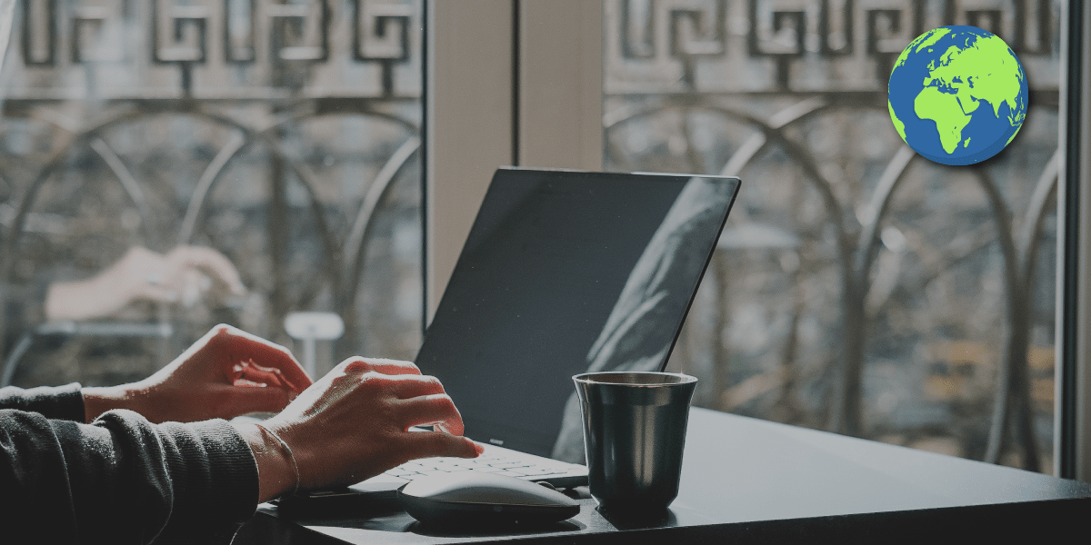 Hands typing on laptop next to mug on desk, globe icon overlay